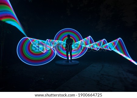 one person standing against beautiful blue green and red circle light painting as the backdrop