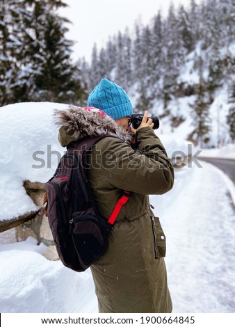 Nature woman landscape photographer in warm clothing  taking picture photos with DSLR camera on Kranjska Gora, Slovenia. Winter activities. Winter holidays. 