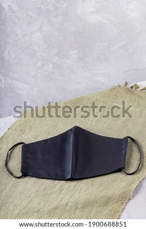 Trendy protective mask on a green cloth. Black face mask on ultimate gray background. Copy space
