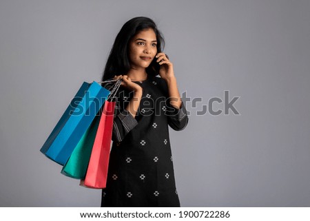 Portrait of a young woman using mobile phone with shopping bags in her hands.