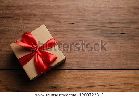 Selective focus of gift box with red ribbon and love shaped paper over rustic wooden table, top view flat lay.