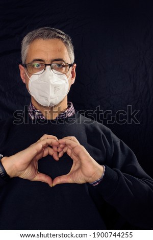 serious man in glasses and mask makes the heart gesture with his hands. black background. vertical format.