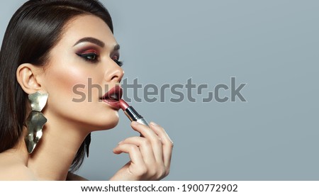 Woman paints lips with shiny lipstick. A dark-haired young woman with smooth skin and bright makeup posing in the studio.