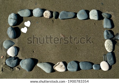 Rectangular frame from stones on beach sand in sunlight with two smal white hearts