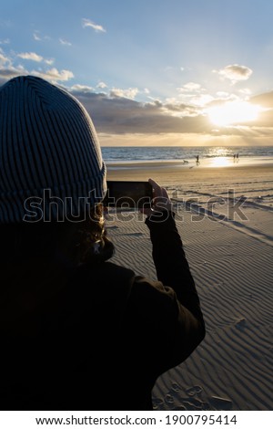 woman taking pictures of the sunset with her smartphone at the beach