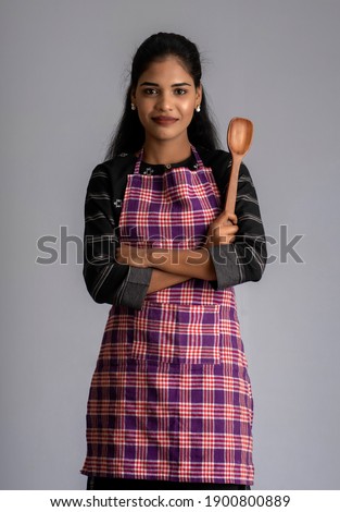 Young girl holding and posing with kitchen utensils spatula on a grey background