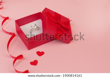 Red box with a white gold ring with a precious stone on a pink background with confetti of red hearts and a red serpentine Royalty-Free Stock Photo #1900814161