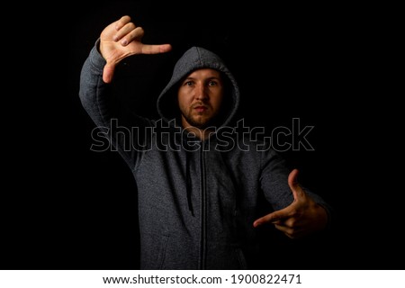 Man in a hood shows the viewer something on a dark background.
