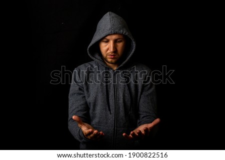 Man in a hood holds something in his hands on a dark background.