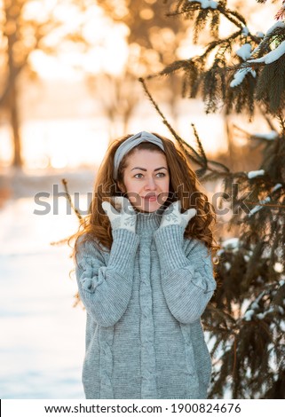 Winter portrait of young beautiful curly brunette woman wearing grey knitted sweater covered in snow. Model looking aside. Snowing winter beauty fashion concept.