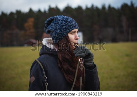 A young breeder in winter clothes blows a dog whistle to summon a stray dog. Authentic people. Binary portrait of girls aged 20-24 whistling at Barbu tcheque, Czech hunting breed. Royalty-Free Stock Photo #1900843219