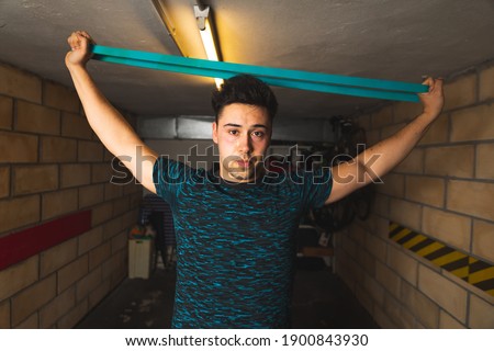 Young caucasian man doing exercise stretching a rope at the garage