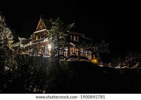 Romantic night picture of famous wooden  mountain shelter at Morskie Oko (Morskie Oko Lake) in High Tatra Mountains, with snowy spruce trees, lit up windows, dark sky, taken on New Year's Eve