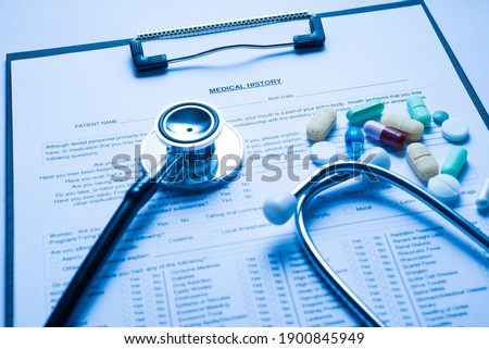 Close up photo of patient history on the clipboard with practitioner's stethoscope and pile stack of colorful different pills