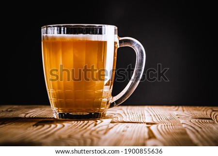glass with draft beer, on a wooden surface, on a dark background. Low key, there is an inscription for the text. Selective focus
