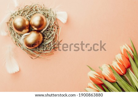 Golden easter colour eggs in basket with spring tulips, white feathers on pastel pink background in Happy Easter decoration. Spring holiday top view concept