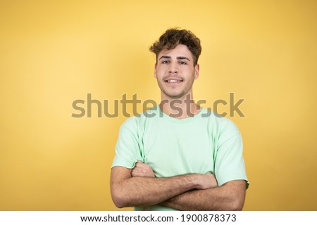 Handsome man wearing a green casual t-shirt over yellow background smiling confident with arms crossed