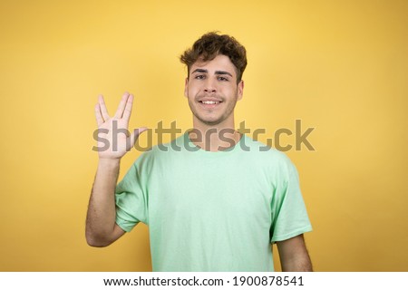 Handsome man wearing a green casual t-shirt over yellow background doing hand symbol