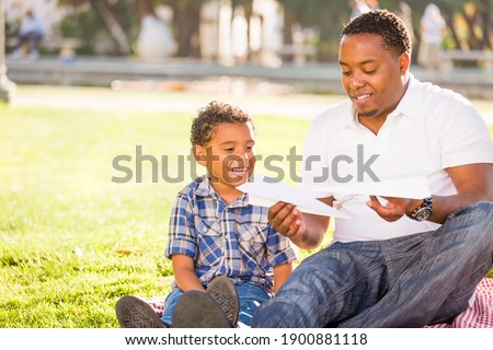 Happy African American Father and Mixed Race Son Playing with Paper Airplanes in the Park Royalty-Free Stock Photo #1900881118
