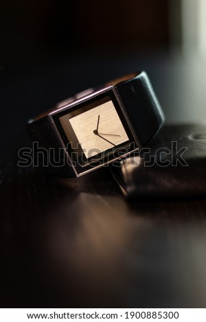 Picture of a square watch without numbers, with a leather strap.