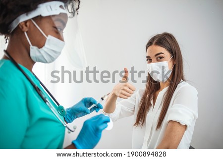 Woman showing thumb up while taking vaccine in medical clinic. Doctor in gloves and face mask holding syringe and making injection to adult female patient. Good advice for illness prevention