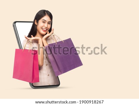 Young smiling beautiful asian woman making online shopping and holding shopping bags out through mobile phone isolated on beige background with clipping path. Royalty-Free Stock Photo #1900918267