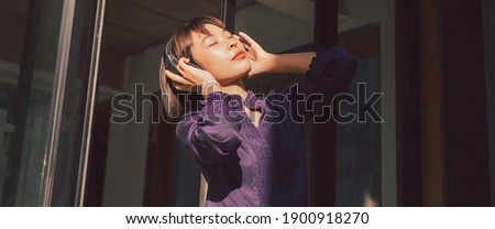 Happy young asian woman listening to music and having fun with headphones on the street. Banner background.