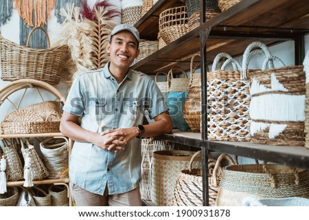 handicraft business owner with his hands leaning back on a shelf while in a handicraft shop with crafts in the shelf background Royalty-Free Stock Photo #1900931878