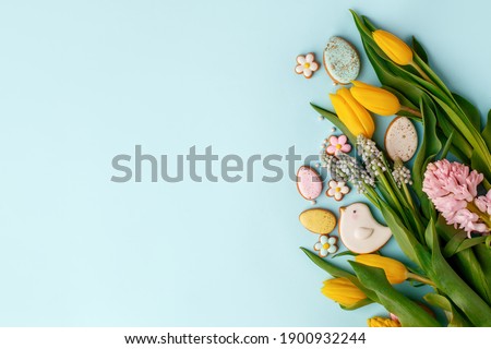 Sweets for celebrate Easter. Gingerbread in shape of easter bunny, flowers and easter eggs, seasonal flowers tulips. Blue background, top view, copy space, banner for your site, flyer, invitation