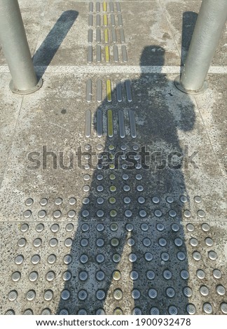 Human shadows seen at the special disability road crossing. The sidewalk has a guide floor for the blind to walk.