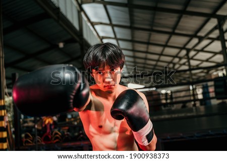 Strong and muscular young man in boxing gear make a hitting motion with the copyspace beside it at boxing training ground background