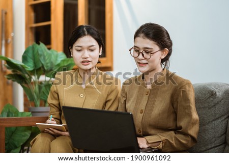 state official and assistant in civil servant uniforms sit together on sofa while working online using laptop in the room