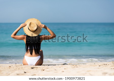 Rear view of woman in bikini resting on the beach in straw hat