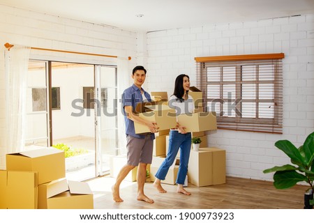 Concept happy moving day and starting a new life for the family : Asian couple, together, holding a cardboard box, marched into their new home with joy excitement.