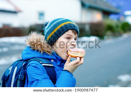 Kid boy eating sweet pie called Kreppel in German or rugelach sufganiyot. Child with cake, religious food for carnival Fasching in Germany or Jewish Chanukka festival