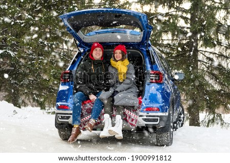 Romantic young hipster couple hugging while sitting in car trunk under falling snow. Love, valentines and holiday concept. Kiss and hug. Valentines day celebration and happiness concept Royalty-Free Stock Photo #1900991812