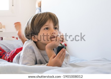 Little Boy Watching Tv.
Cute Little Boy Resting On Bed Mesmerized And Relaxing While Watching Tv.