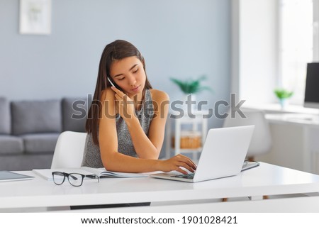 Asian woman talking on phone using office laptop computer. Personal business assistant or magazine editor browsing web, booking tickets online, entering order into database or planning boss's schedule