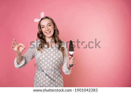 young charming woman pastry chef with a spatula in her hands. A cook in a polka-dot apron. pastry chef in an apron on a pink background.