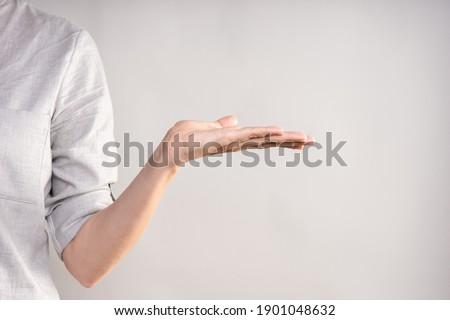 Elegant female hand, pointing to the side. palm holds something, a blank for the design. businesswoman in a casual gray shirt makes a hand gesture
