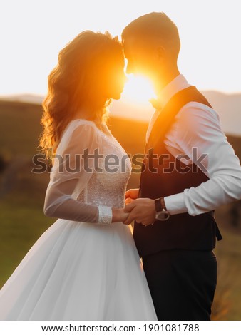 Beautiful couple stand facing each other holding hands on a background of sunset. Romantic silhouettes.