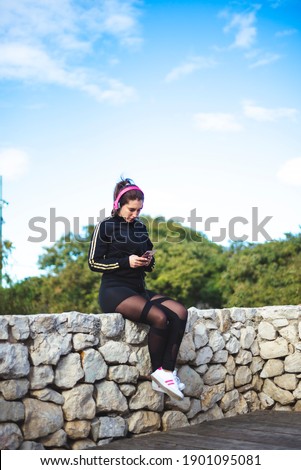 Portrait of a sporty young woman with headphones and phone sit at park. 