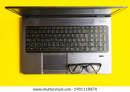 top view of eyeglasses and laptop or mobile workstation on yellow background.concept need to wear glasses. work space. flat lay