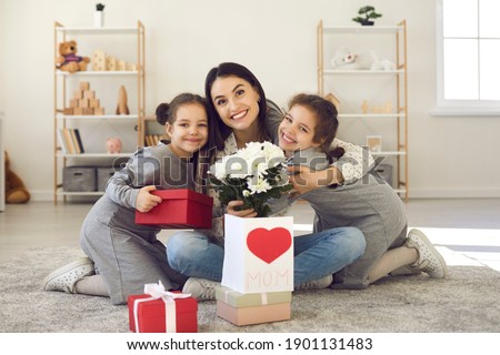 We love you, mom. Kids hugging mommy and giving her presents and greeting card on Mother's Day. Portrait of happy young woman with flowers embracing her little children, smiling and looking at camera