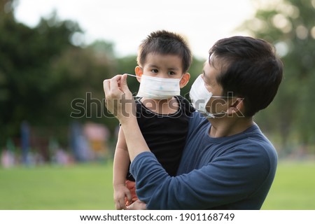 Asian father is wearing the face mask to his little son to protect for Covid-19 and pm 2.5 for outdoor activity in the public place, concept of healthcare and safety for kid in virus outbreak.