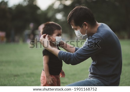 Asian father is wearing the face mask to his little son to protect for Covid-19 and pm 2.5 for outdoor activity in the public place, concept of healthcare and safety for kid in virus outbreak. Royalty-Free Stock Photo #1901168752