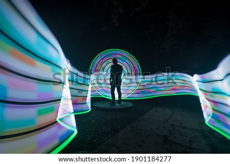 one person standing against beautiful blue green and white circle light painting as the backdrop