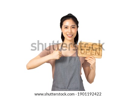 Beautiful young asian woman smiling pretty teeth wearing a apron.Woman holding a wooden sign pointing and thumbs up