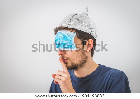 Young angry man with face mask over the eyes and aluminum hat is doing a psst! gesture Royalty-Free Stock Photo #1901193883