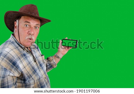 An old farmer is clearly disappointed while holding a smartphone with a chroma key copy space screen in his hand. Taken on a green background.